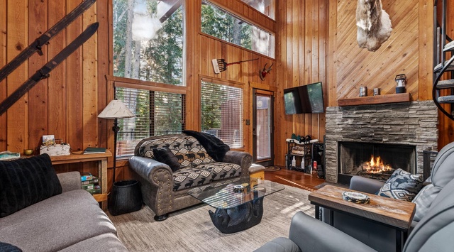 Cozy up by the crackling fireplace in this rustic living room, where warm wood walls and comfortable seating create your perfect mountain retreat.