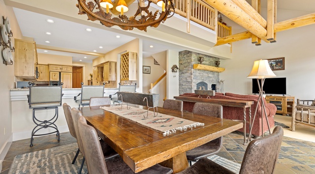Gather around the stunning wood dining table under a rustic chandelier, with your cozy living room and stone fireplace just steps away—perfect for memorable evenings together.