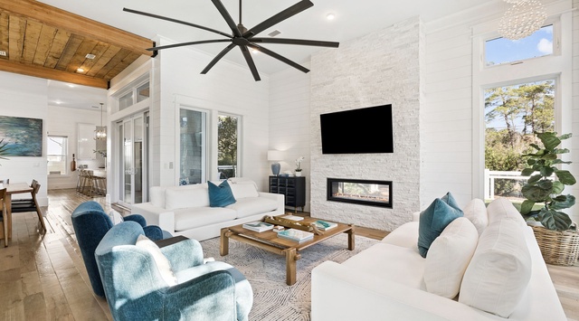 Sink into plush white sofas by the modern fireplace, where coastal blue accents and warm wood beams create your perfect retreat.