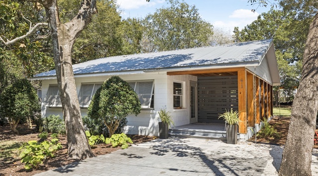 Modern eco-friendly cottage with solar panels, nestled among mature trees in a peaceful neighborhood setting.