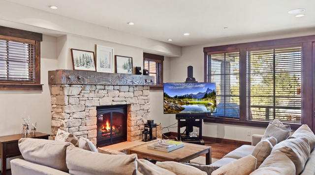 Curl up on plush sofas by the warm stone fireplace, where soft natural light filters through wooden blinds and mountain views frame your perfect evening retreat.