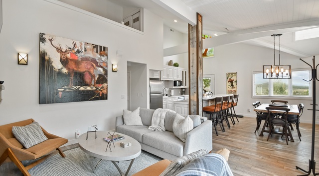 Relax in this airy open-concept living space, where modern comfort meets rustic charm with soaring ceilings, natural wood accents, and seamless flow to the dining and kitchen areas.