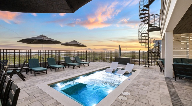 A rooftop terrace with a plunge pool, lounge chairs, and spiral staircase overlooks the horizon. The property is situated in a scenic coastal area with views of distant landscapes and colorful sunsets.