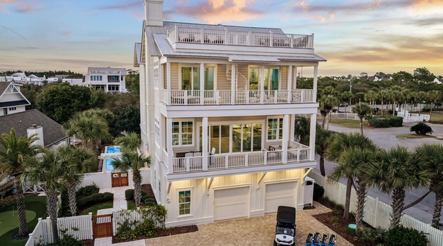 Stunning three-story coastal home with multiple balconies and roof deck, surrounded by palm trees in a picturesque neighborhood setting.