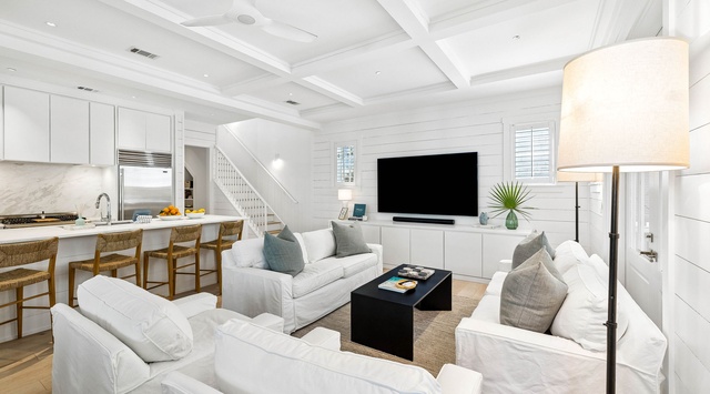 Sink into plush white sofas and unwind in this beautifully designed open-concept space. Coastal elegance meets modern comfort with soaring coffered ceilings, natural light, and a thoughtfully appointed kitchen just steps away.