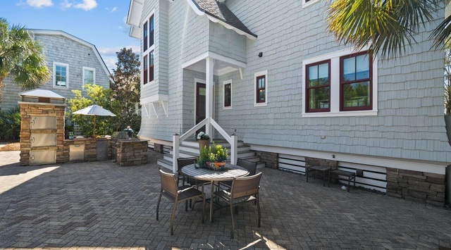 Charming coastal retreat featuring weathered shingle siding, tropical palms, and your own private patio with stone accents and outdoor dining space.