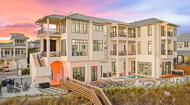 Stunning beachfront property with dramatic sunset colors painting the sky above this luxurious coastal home, featuring multiple balconies and oceanfront access.