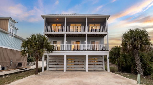 Coastal vacation home with palm trees and covered parking beneath spacious multi-level balconies.