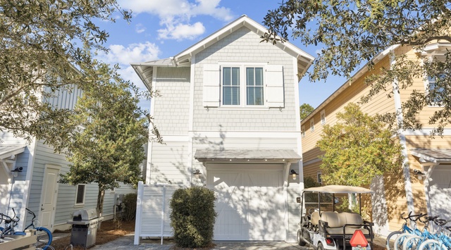 Charming white cottage with blue shutters nestled among mature trees in a peaceful residential setting.