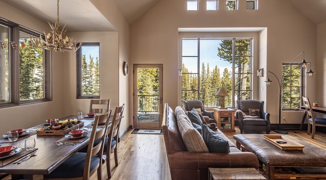 Relax in this stunning open-concept living space where rustic leather furnishings meet soaring ceilings and floor-to-ceiling windows showcase breathtaking forest views.