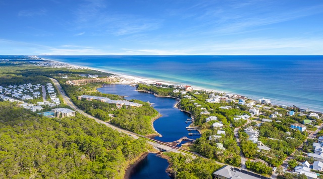 Stunning aerial perspective of pristine coastline with azure waters meeting white sand beaches, surrounded by lush forests and charming coastal community.