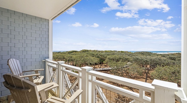 Picture yourself unwinding on your private balcony, where comfortable seating overlooks lush coastal greenery stretching toward the sparkling turquoise shoreline in the distance.