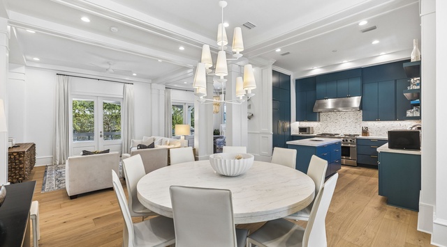 Bright, open-plan living space featuring a marble-topped dining table, tall windows flooding the area with natural light, and a fully-equipped kitchen with sleek cabinetry and premium appliances.