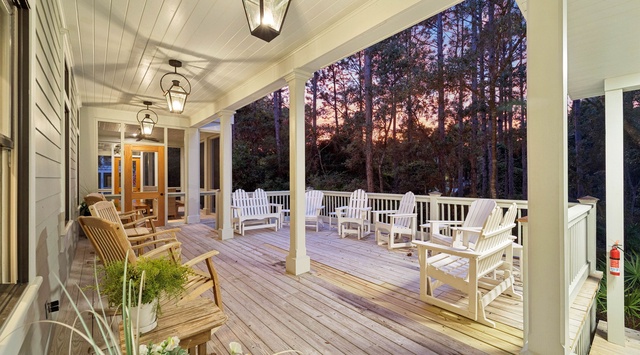 A spacious covered porch welcomes you with classic white rocking chairs and warm lantern lighting, overlooking tranquil wooded surroundings—perfect for your morning coffee or evening unwind.