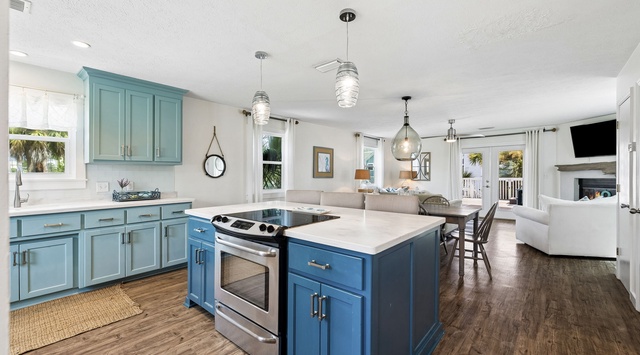 Step into your coastal retreat, where soft blue cabinetry and warm wood floors create an inviting open layout. Cook, gather, and unwind as natural light streams through oversized windows, connecting you to the tropical views beyond.