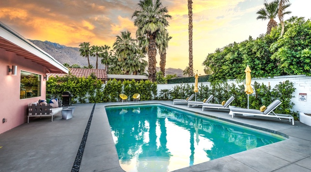 A stunning desert oasis set against dramatic mountain scenery. Your private pool sparkles under golden hour skies, surrounded by swaying palms and modern lounge chairs—perfect for soaking up the California sunshine.