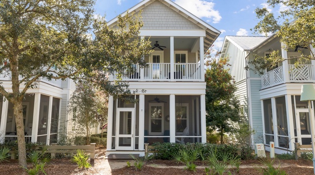 Charming coastal cottage with classic architecture, front porch, and mature oak trees in a peaceful residential setting.