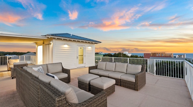 A rooftop terrace overlooking the ocean at sunset, featuring comfortable outdoor seating arranged for gatherings in the warm evening light.