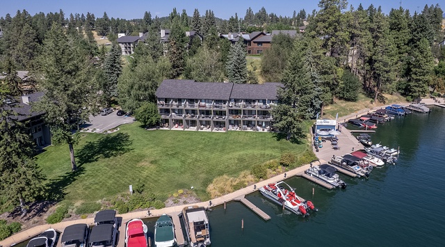 Aerial view of a waterfront vacation property nestled among towering pines, featuring private boat docks on serene lake waters and expansive green lawns for relaxation.