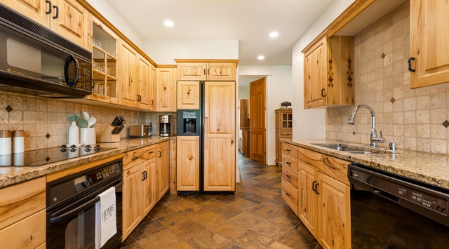 Fully equipped kitchen with warm wood cabinets and granite counters, modern appliances, and ample prep space perfect for gathering and cooking together.
