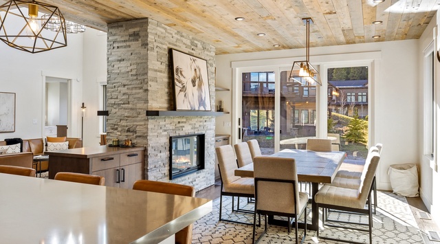 Gather around the handsome stone fireplace at your farmhouse dining table, where warm wood tones and abundant natural light make every meal feel special.