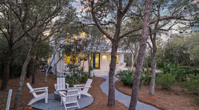 Charming coastal cottage nestled among towering trees with a welcoming entrance and peaceful outdoor seating area.