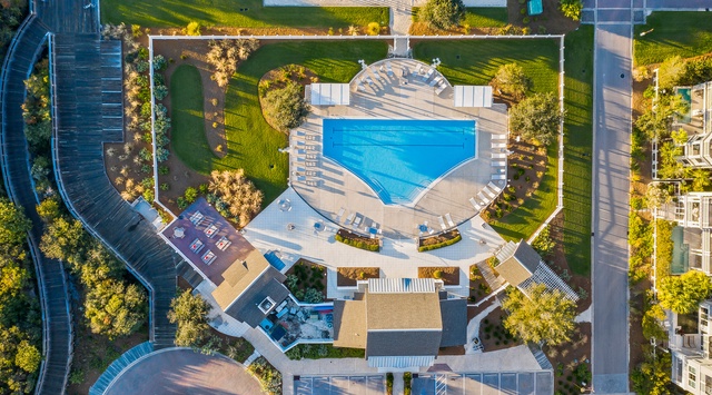 An aerial view captures the property's impressive layout, featuring a sparkling pool surrounded by lush landscaping and manicured lawns. A picnic and lounge area with sun chairs invites relaxation under golden afternoon light.