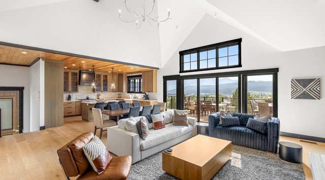 Bright open-concept living space with soaring vaulted ceilings, mountain views, and floor-to-ceiling windows flooding the room with natural light.