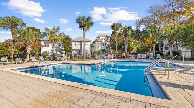 Community pool area with tropical landscaping and residential buildings surrounded by palm trees.