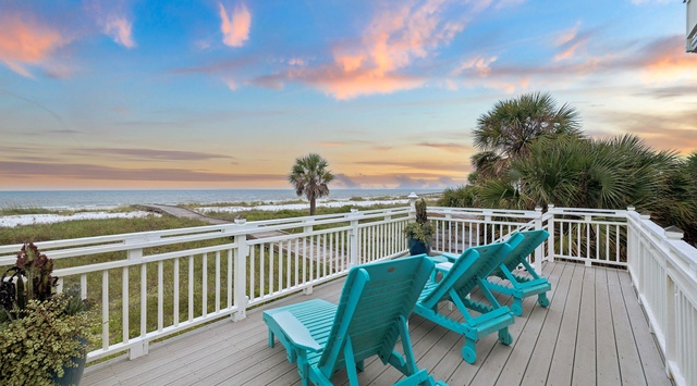 Expansive deck overlooking sandy shoreline and native palms, where soft pastels paint the evening sky over coastal dunes—a stunning backdrop for the surrounding area.