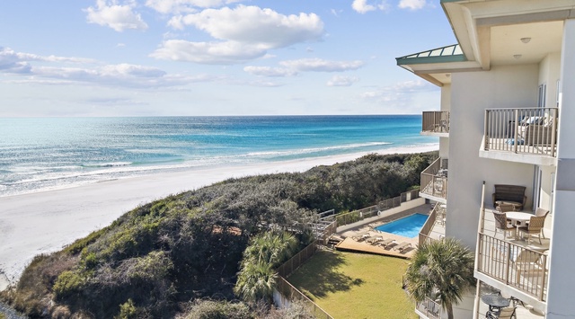 Oceanfront property overlooking pristine white sand beaches and turquoise waters, featuring multiple balconies and a private pool area surrounded by coastal vegetation.