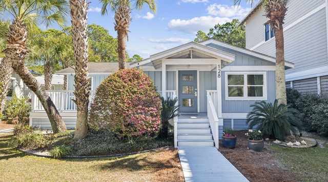 Charming coastal cottage framed by towering palms and colorful tropical landscaping in a peaceful residential neighborhood.