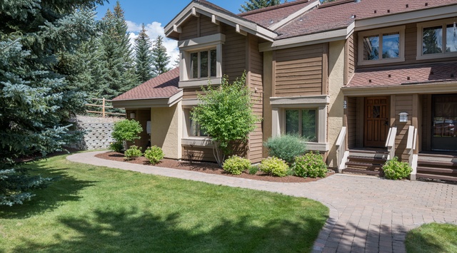 A charming mountain-style property surrounded by towering evergreens and manicured landscaping, offering a peaceful retreat in a beautiful natural setting.