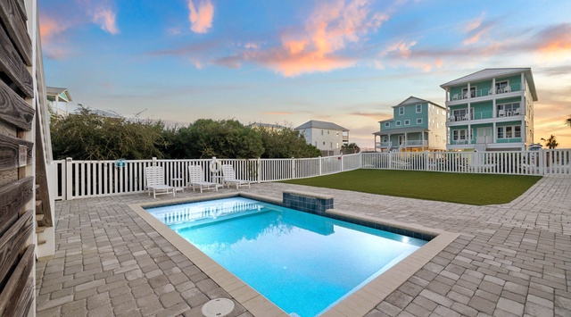A private swimming pool awaits beneath a stunning sky painted in soft oranges and blues. Lounge on the deck chairs and soak in the peaceful coastal evening as the day winds down.