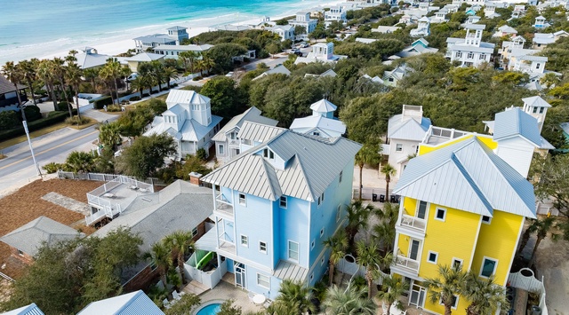 Aerial view of colorful beach houses nestled among palm trees, just steps from pristine white sand and turquoise waters.