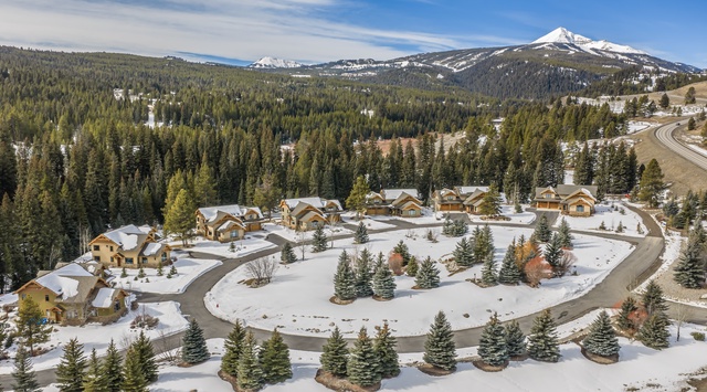 Mountain retreat community with cabins nestled among snow-covered evergreen forests and dramatic alpine peaks.