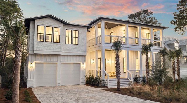 Modern two-story coastal home with elegant architectural design, featuring warm lighting and tropical landscaping in a serene neighborhood setting.