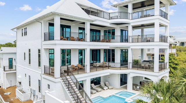 Elegant white multi-story vacation home featuring multiple private balconies, stunning pool area, and tropical landscaping in a peaceful residential setting.