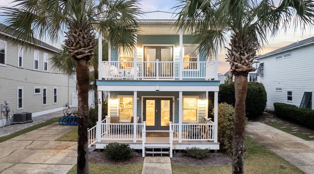Charming coastal cottage with double-decker porches framed by swaying palms in peaceful neighborhood setting.