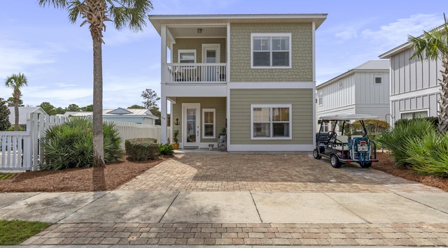 Charming two-story beach home with tropical palm trees and brick driveway featuring golf cart parking in coastal neighborhood.
