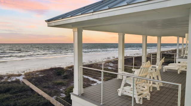 Expansive beachfront deck with Adirondack chairs overlooks pristine coastline during stunning sunset hours.