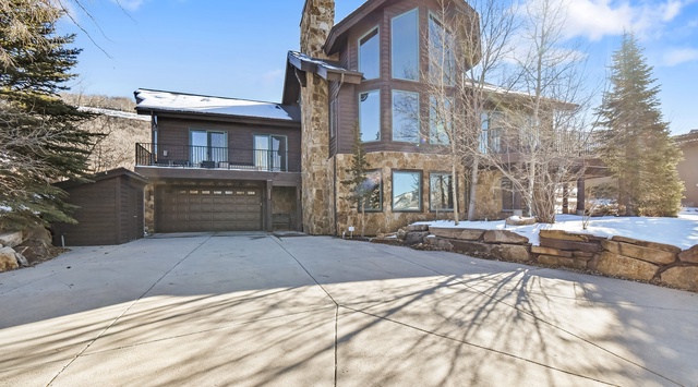 Contemporary mountain home featuring stone and wood architecture with expansive windows and dedicated parking.
