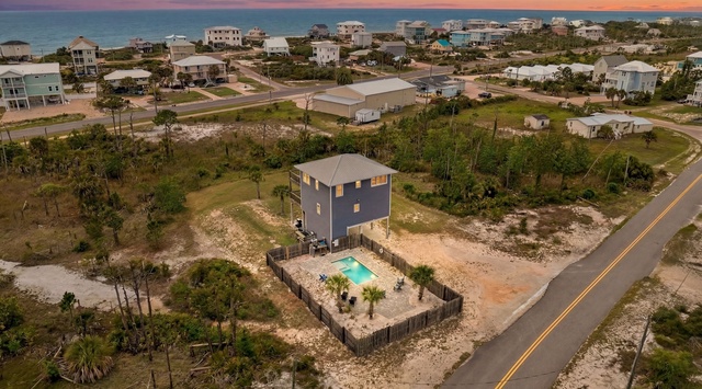 Aerial view of coastal vacation home with private pool, moments from the beach, framed by palms and a vibrant sunset over the Gulf.