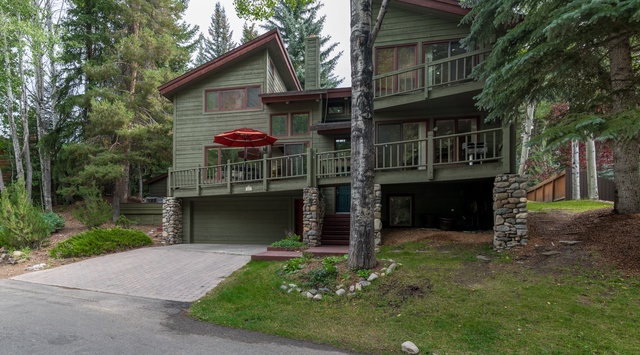 A charming mountain retreat nestled among towering pines and birch trees, featuring spacious decks and stone accents that blend seamlessly with the natural forest surroundings.