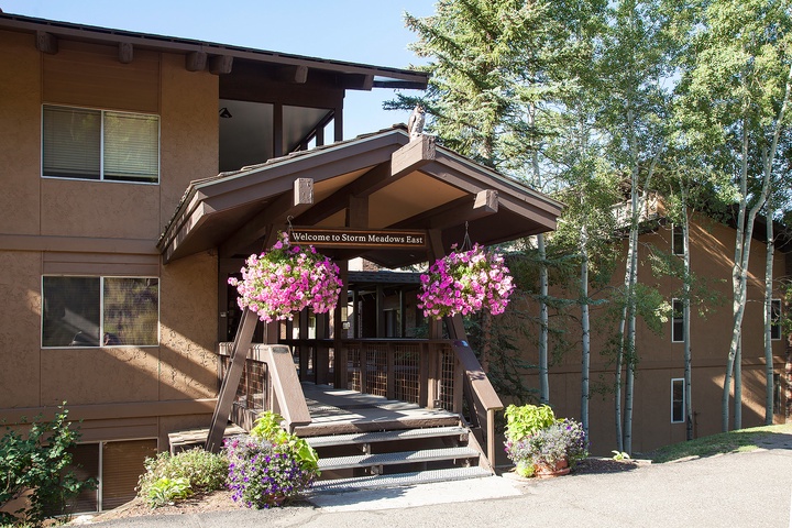 The welcoming entrance to Storm Meadows East, framed by vibrant hanging flower baskets and surrounded by mature trees, marks the arrival point to the property.