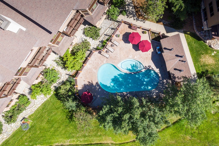 Aerial view showcases a stunning kidney-shaped pool surrounded by lush lawns, vibrant umbrellas, and comfortable sun loungers, all nestled within beautifully landscaped gardens beside the main building.