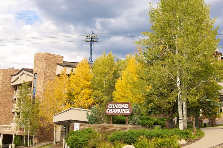 Chateau Chamonix property entrance surrounded by vibrant autumn aspens and evergreens, set against dramatic mountain skies and residential buildings.