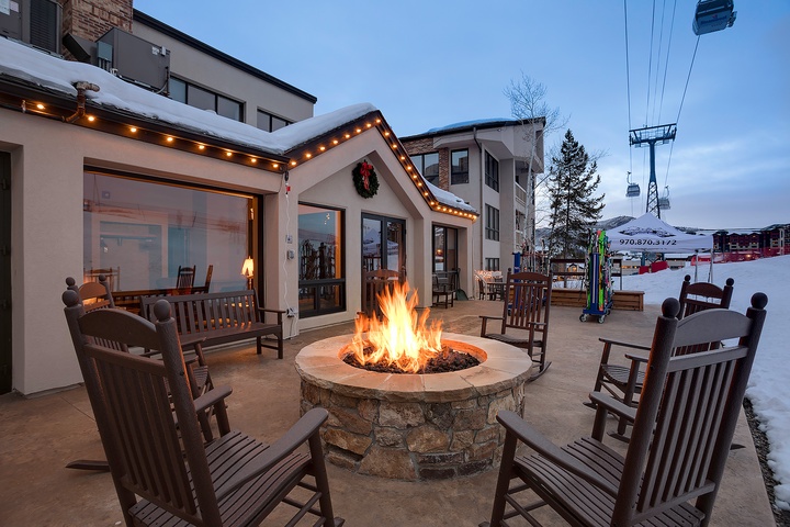 The property features a cozy stone fire pit surrounded by wooden rocking chairs on a spacious patio, offering a charming gathering spot near ski lifts and mountain slopes.