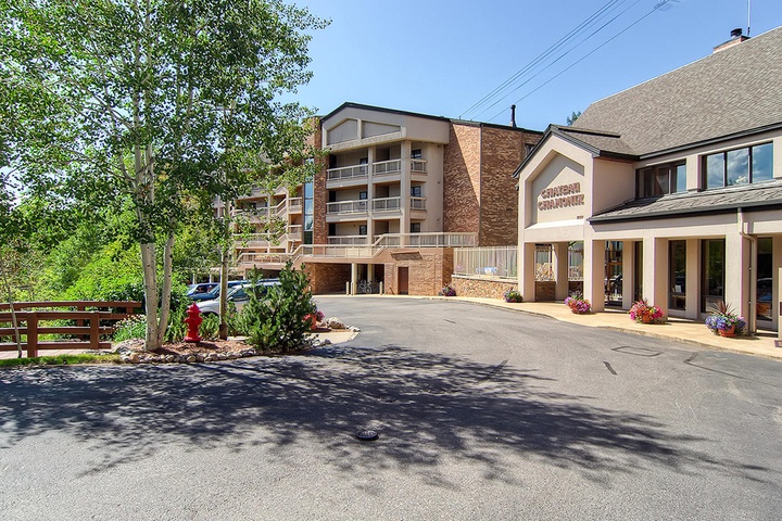 The property entrance features a multi-story lodge-style building with convenient parking and landscaped surroundings, located in a peaceful mountain setting with nearby trees and scenic views.