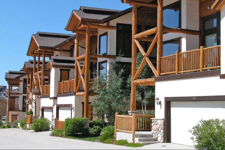 Charming alpine-style property featuring warm timber balconies and white stone accents set against a clear blue sky.